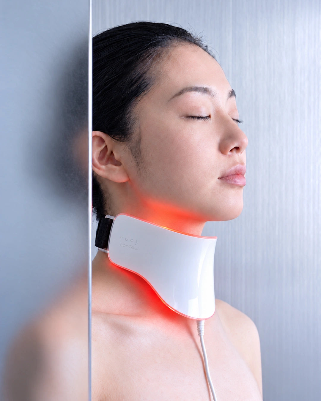 Masque LED nuaj. contour porté autour du cou, gravure latérale, coque nacrée, sangle noire et lumière rouge, devant un miroir argent